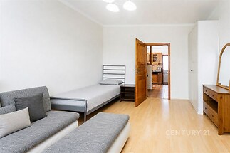 Světlý obývací pokoj s parketovou podlahou, vestavěné skříně a moderní nábytek. Ložnice je částečně oddělena.