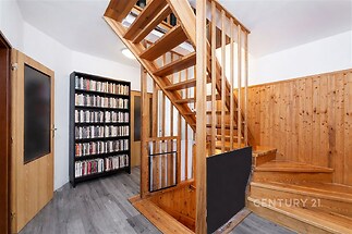 Chodba se schodištěm z masivního dřeva, vinylová podlaha a dřevěné obložení stěn, moderní design s velkou knihovnou.