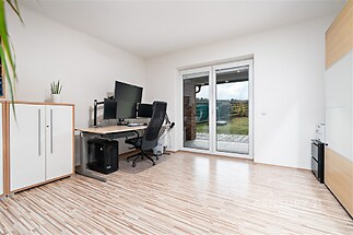 Pracovna s moderní laminátovou podlahou, velká okna poskytující výhled do zahrady, vestavěné úložné skříně, světlý prostor.