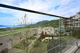 Balkón s proskleným zábradlím nabízí výhled na hory a mořem, moderní architektura budov s terasovým designem, ideální pro relaxaci.