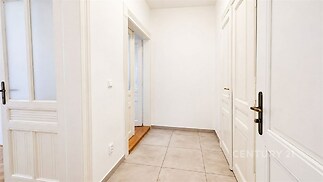 Vstupní hala s dlažbou, bílými dveřmi a moderním designem poskytuje světlý a elegantní prostor v rekonstruovaném bytě.