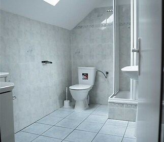Světlá koupelna s dlažbou a sprchovým koutem, střešní okno, moderní vybavení, světlé kachličky vytvářejí čistý a prostorný dojem.