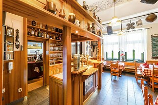 Restaurace s dřevěným interiérem, dlažbou a velkými okny, zachovávající tradiční styl s dekorativními prvky a útulným posezením.