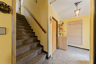 Vstupní hala s kamennou dlažbou, světlé stěny a dekorativní osvětlení, vedle schodiště a dřevěného věšáku, působí jako útulný prostor v rekonstruovaném domě.