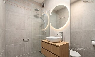 Moderní koupelna s minimalistickým designem, velkoformátové dlaždice, kulaté osvětlené zrcadlo a dřevěná skříňka pro elegantní vzhled.