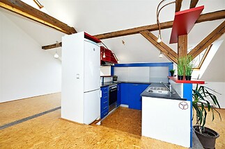 Moderní kuchyň v podkroví s modrými skříňkami a vestavěnými spotřebiči. Dřevěné trámy a parketová podlaha dodávají rustikální kouzlo.