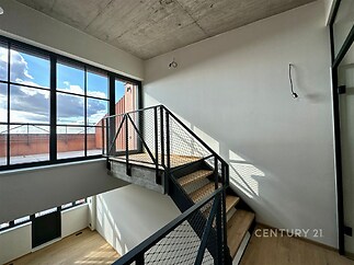 Schodiště s moderním designem, dřevěné stupně a kovové zábradlí, velká okna zajišťující světlé a prostorné prostředí, industriální styl.