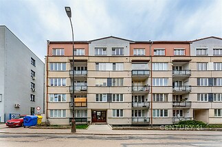 Čtyřpatrový bytový dům s balkony, moderní fasáda, velká okna, městská lokalita, parkování před domem.