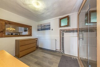 Malá místnost s dřevěným nábytkem, plovoucí podlahou a velkým zrcadlem. Vhodná pro úložné prostory, nabízí světlý a praktický interiér.