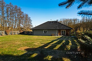 Rodinný dům s černou střechou na prostorném pozemku, obklopený upravenou zahradou. Nachází se v klidné části s výhledem na les.