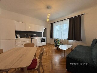 Moderní obývací pokoj s parketovou podlahou, velkými okny a světlým nábytkem nabízí pohodlné a stylové bydlení.