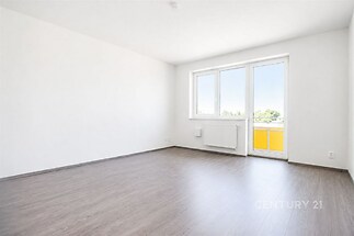 Světlý obývací pokoj s moderní parketovou podlahou a velkými okny, bílými stěnami a balkonem.