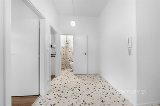 Světlá vstupní hala s moderní dlažbou, bílými zdmi a minimalistickým osvětlením, ideální pro rekonstruované interiéry.