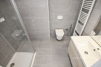 Moderní koupelna s šedou dlažbou, sprchovým koutem a závěsnou toaletou, stylová umyvadlová skříň a topný žebřík.