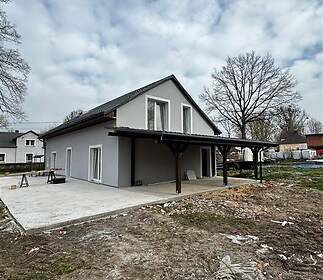 Moderní rodinný dům s šedou fasádou a velkou terasou, zahrnující novou střechu a dvojitá francouzská okna, nacházející se na travnatém pozemku