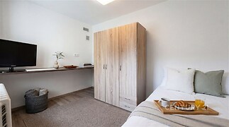 Světlá ložnice s parketovou podlahou a vestavěným pracovním stolem, moderní šatní skříň, útulné vybavení a minimalistický styl.