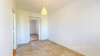 Světlý pokoj s parketovou podlahou, moderní svítidlo a čerstvě vymalované stěny, jednoduchý vstup do další místnosti.