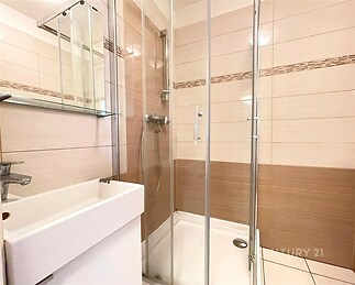 Moderní koupelna, sprchový kout s čirým sklem, dlažba ve světlých tónech, elegantní umyvadlo, stylový a čistý design.