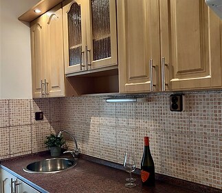 Kuchyňská linka s dřevěnými skříňkami, dlažba na stěně, moderní osvětlení pod linkou, pracovní deska z kamene, myčka Bosch