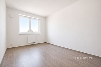 Světlá ložnice s moderní parketovou podlahou, velkým oknem a bílými stěnami, nabízí prostor pro vestavěné skříně a je ve výborném stavu.