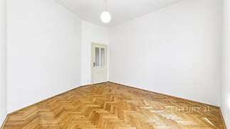 Prázdný pokoj s parketovou podlahou, bílými stěnami a vysokým stropem, vhodný pro rekonstrukci nebo moderní úpravy.