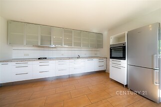 Prostorná a světlá kuchyň s moderními vestavěnými spotřebiči, dřevěnou podlahou a skříňkami s matnými skleněnými dvířky.