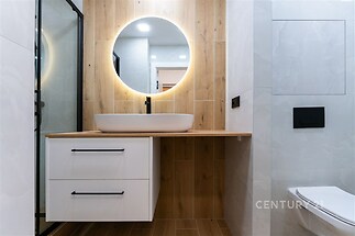 Moderní koupelna s dřevěnými obklady, vestavné umyvadlo a kulaté osvětlené zrcadlo, elegantní minimalistický design