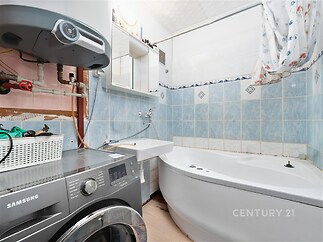 Malá koupelna s rohovou vanou, světlé dlaždičky s modrými akcenty, pračka, zrcadlová skříň v retro stylu, útulné rozvržení.