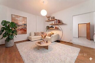 Světlý obývací pokoj s parketovou podlahou, moderní nástěnnou dekorací a velkým kobercem, nabízí útulné posezení a elegantní styl.
