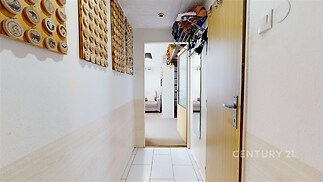 Úzká chodba s dlažbou, dekorativními prvky na stěnách a moderními dveřmi vede do světlého obývacího pokoje s velkými okny.