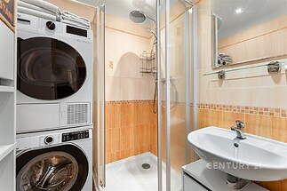 Kompaktní koupelna s moderním sprchovým koutem, dlažbou a pračkou se sušičkou, světlé obklady dodávají místnosti moderní vzhled