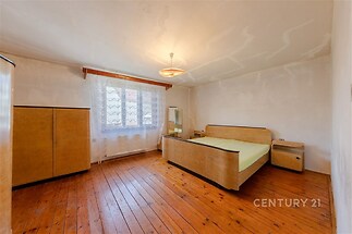 Prostorná ložnice s dřevěnou podlahou, velkými okny a starožitným nábytkem, ideální pro rekonstrukci, nabízí světlý a útulný prostor.