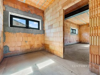 Nedokončená místnost s velkými okny, cihlové zdi a betonová podlaha, vhodná pro rekonstrukci, nabízí moderní vzhled a flexibilitu prostor