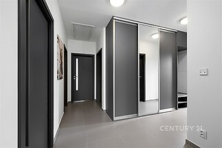 Chodba s velkými vestavěnými skříněmi, moderními dveřmi a dlažbou. Světlý prostor s minimalistickým designem.