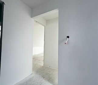 Prázdná místnost s bílými zdmi, betonová podlaha, otevřený průchod, moderní styl, příprava na elektroinstalaci, vhodné pro úpravy.