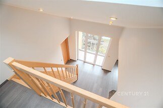 Světlé schodiště s dřevěným zábradlím, vzdušný prostor, moderní interiér s velkými okny, šedá dlažba, přístup na balkon nebo terasu.