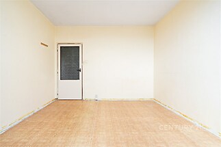 Prázdný pokoj s parketovou podlahou, světlé stěny, jednoduché dveře, ideální pro rekonstrukci a úpravy dle vlastního stylu.