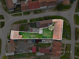 Pohled z ptačí perspektivy na pozemek s dvěma stavbami a zahradou, umístěný v klidné rezidenční oblasti s červenými střechami domů.