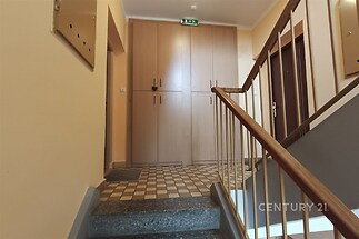 Společná chodba bytového domu, vestavěné skříně, dlažba s geometrickým vzorem, jednoduché zábradlí, světlé stěny.