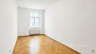 Světlý pokoj s parketovou podlahou, bílými stěnami a velkým oknem, ideální pro moderní interiérové úpravy.