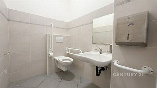 Bezbariérová koupelna s moderními obklady, závěsnou toaletou a umyvadlem, doplněná o nerezové madla pro zvýšenou bezpečnost a komfort.