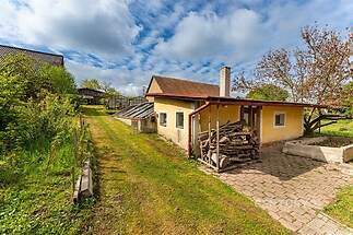 Malý venkovský dům s dřevěným přístavkem, dlážděná terasa, obklopený zahradou, ideální pro rekreační využití v klidné lokalitě.