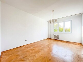 Světlý obývací pokoj s parketovou podlahou, velká okna zajišťující dostatek denního světla, bílá malba vytvářející moderní vzhled