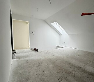 Podkrovní místnost s velkým střešním oknem, šikmý strop, neutrální barvy, příprava na rekonstrukci, potenciál pro vestavěné skříně.