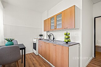 Kuchyň s dřevěnými skříňkami, parketovou podlahou a moderním designem. Světlá místnost s jídelním stolem a vestavěnými spotřebiči.