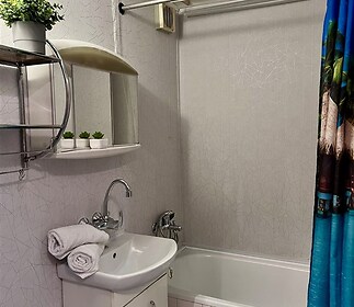 Kompaktní koupelna s vanou, dlažbou a moderním umyvadlem, vybavená zrcadlovou skříňkou a dekorativními rostlinami.