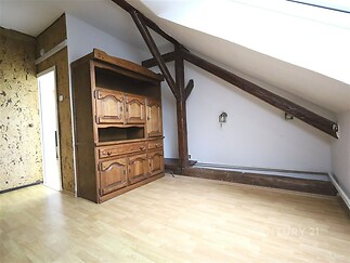 Podkrovní pokoj s dřevěnou skříní a parketovou podlahou, velké střešní okno přináší přirozené světlo, stěny v rustikálním stylu.