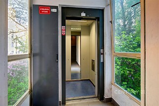 Vstupní hala s moderním výtahem, dlažba na podlaze a velkými okny poskytujícími výhled do zeleně, světlý a udržovaný prostor