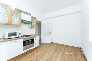 Moderní kuchyň s dřevěnou podlahou, vestavěnými spotřebiči a světlými štíty, prostorná místnost ideální pro rodinné vaření.