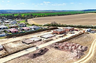 Staveniště rodinných domů na venkově, rozestavěné budovy a stavební pozemek, výhled na pole a zelené okolí, ideální pro bydlení v přírodě.